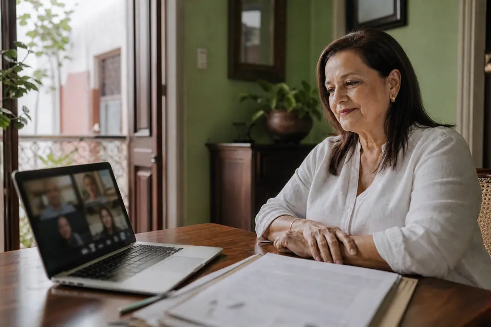 Mujer revisa documentos de herencia frente a su computadora durante una videollamada familiar