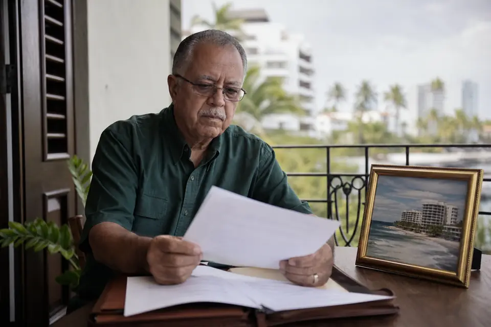 Hombre mayor revisa documentos en un balcón junto a la foto de un apartamento