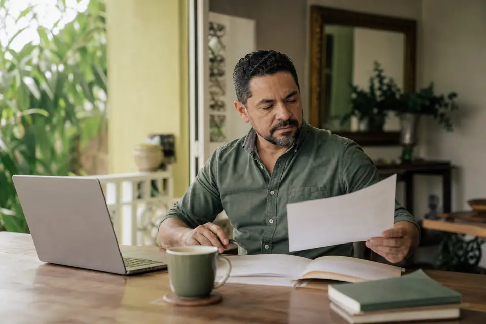 Hombre prepara documentos familiares en su computadora en un escritorio de su casa
