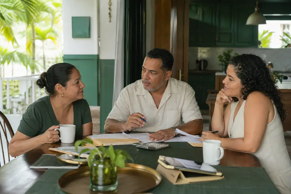 Tres hermanos conversan en la cocina con carpetas sobre cómo dividir la herencia